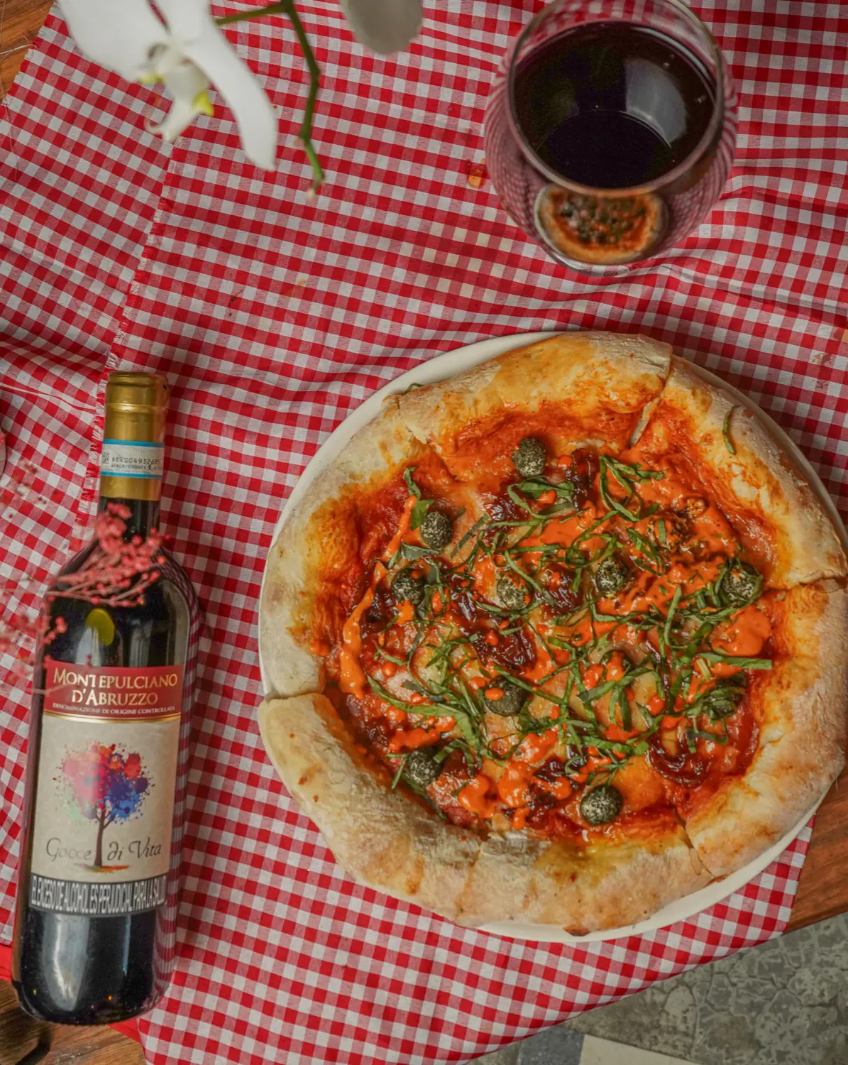 Pizza Caprina y una botella de vino tinto sobre un mantel a cuadros rojos
