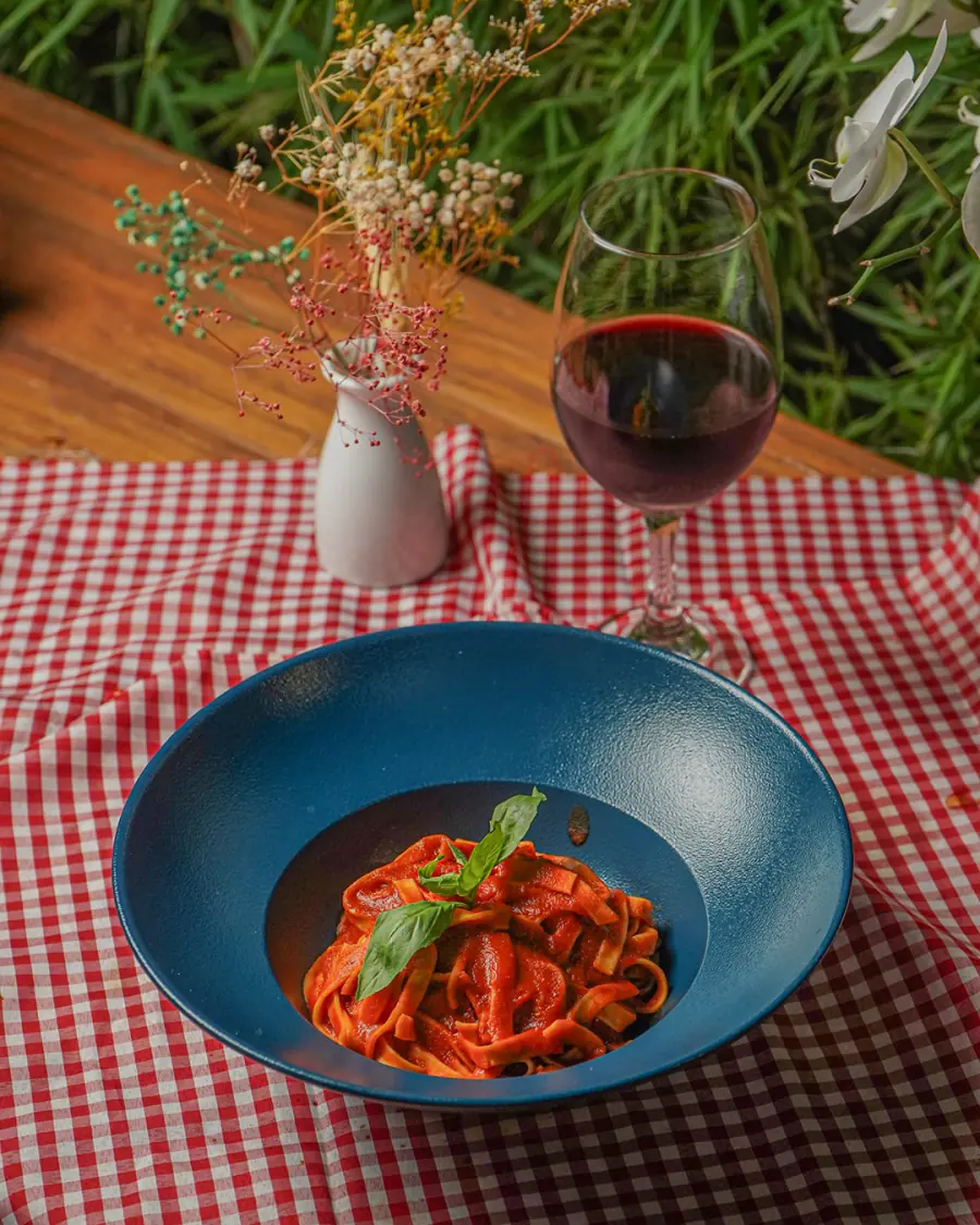 Pasta pomodoro y copa de vino tinto en una mesa de la terraza, con plantas al fondo